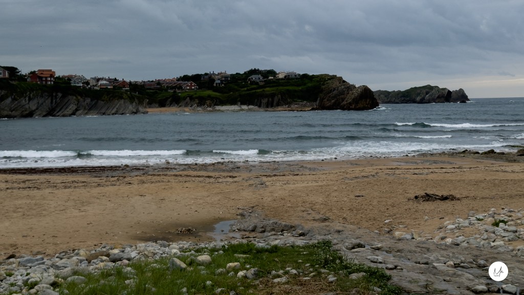Playa de Valdearenas con arena, rocas y horizonte marino bajo nubes.
