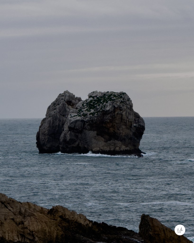 Roca aislada en el mar Cantábrico bajo cielo grisáceo.