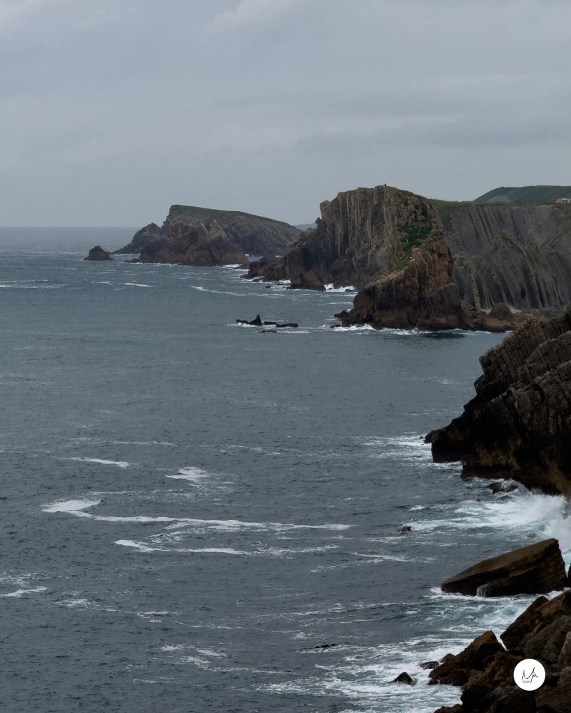 Acantilados y olas rompiendo en Cernía bajo cielo gris.