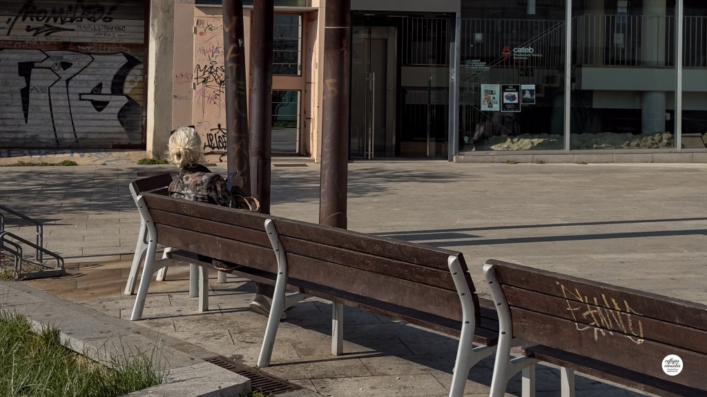 Mujer sentada sola en un banco revisando su teléfono móvil.